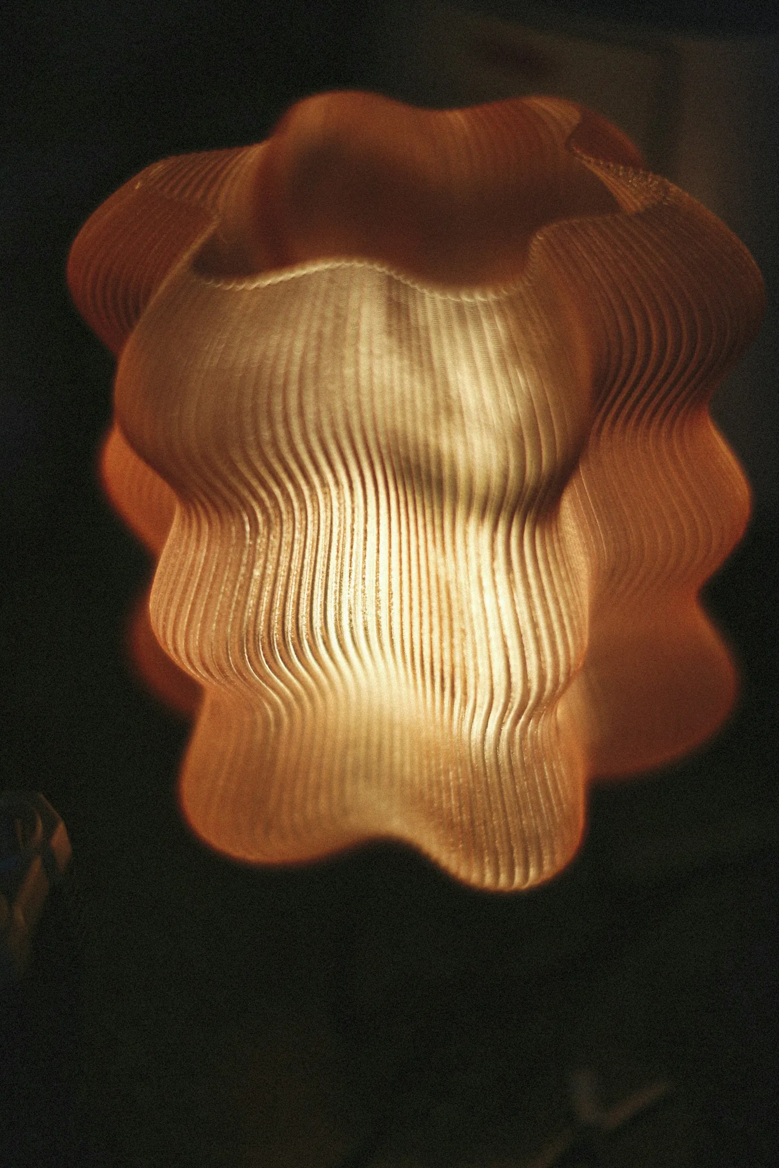 Luminária orgânica impressa em 3D, com luz quente atravessando as camadas